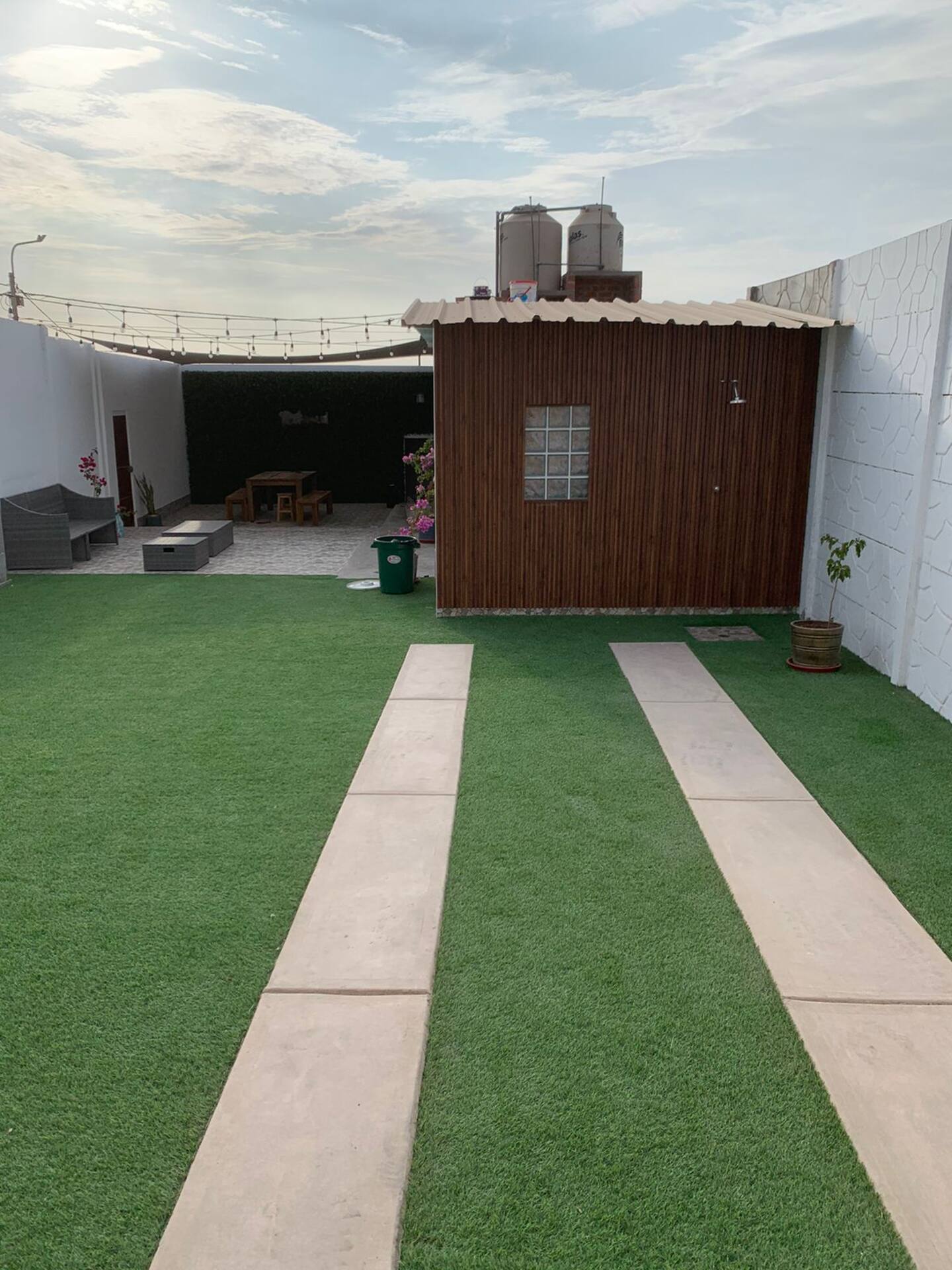 Jardín amplio con césped, caminos y ducha exterior de madera